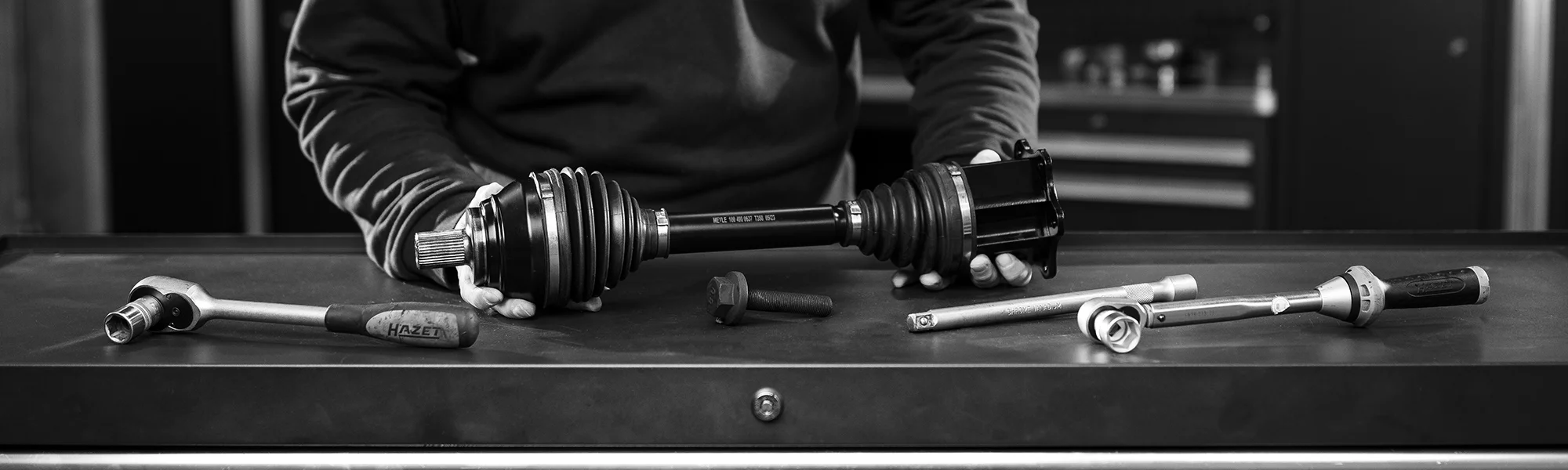 Auto-Mechaniker hält Antriebswelle, Werkzeuge auf Werkbank, meyle.com DriveTrain.