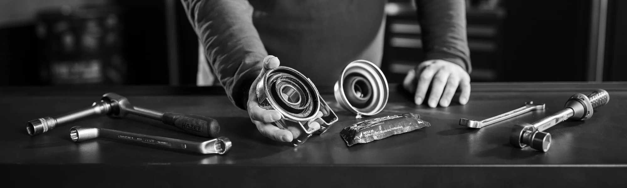Mechaniker präsentiert Kardanwellen-Reparaturkit neben Werkzeugen auf Werkbank.