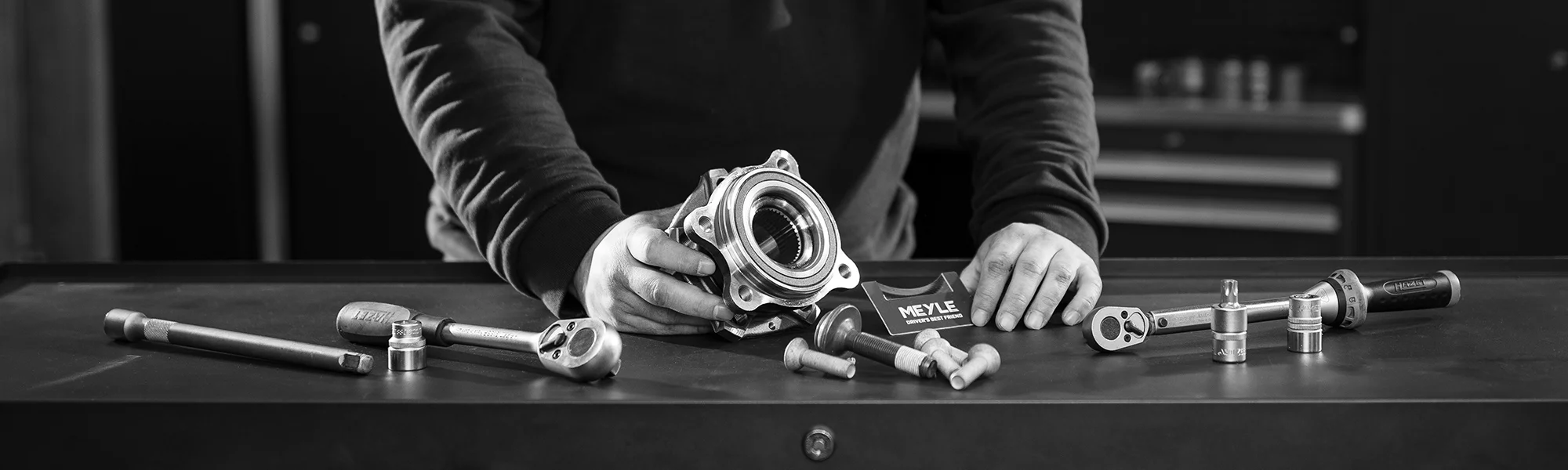 Mechaniker präsentiert Radnaben-Reparaturset mit Werkzeugen auf Werkbank, meyle.com DriveTrain Werbebild.