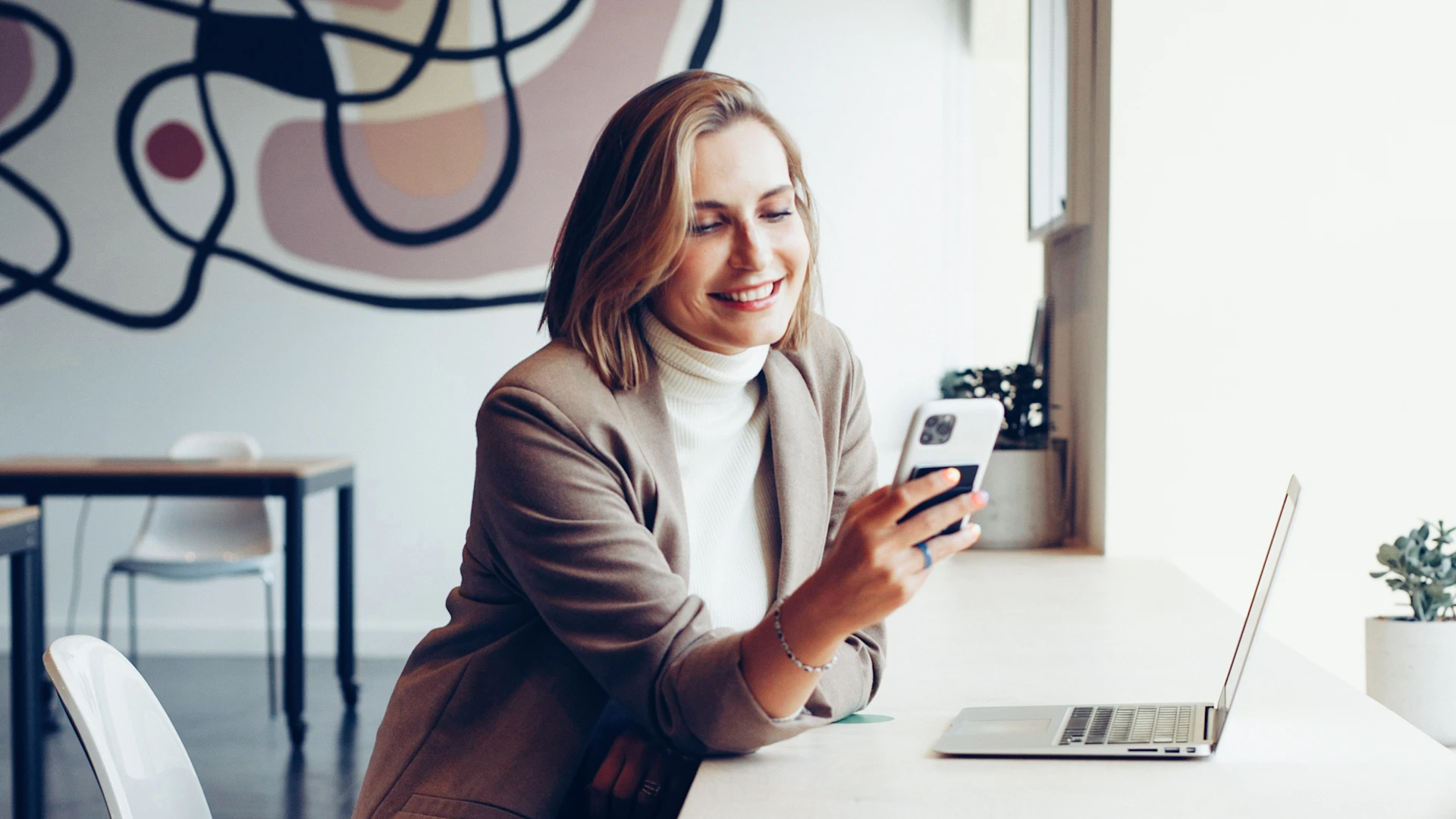 A happy person with a smart phone in their hand and a laptop in front of them.