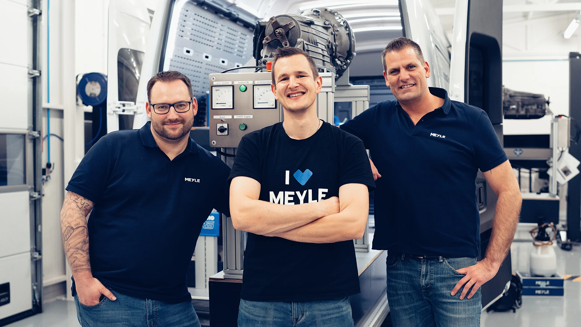 Three MEYLE trainers stand in front of their training van and smile into the camera.