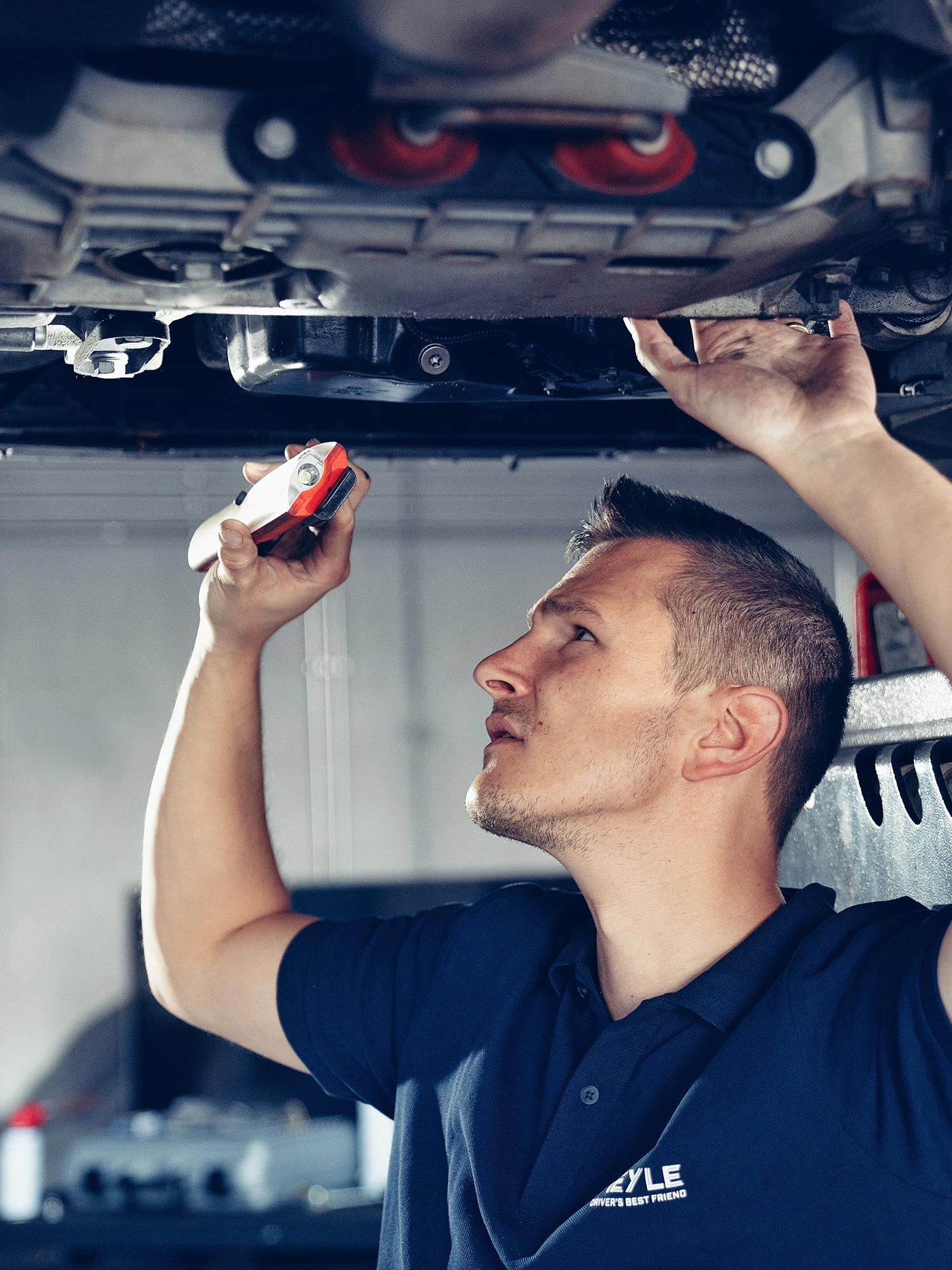 Mechanic stands under a car on the lift and takes a close look at a drive part.