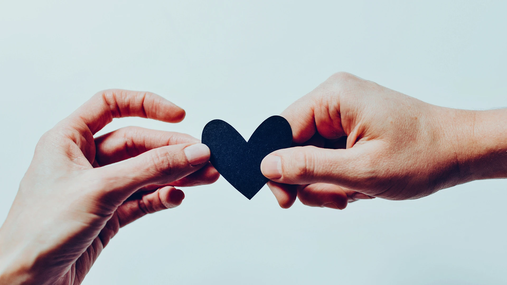 Two hands hold a black paper heart.