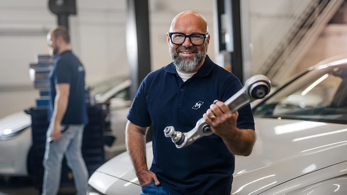 The well-known German mechanic Andreas Raulfs is standing in front of a car, holding a MEYLE HD handlebar and smiling into the camera.