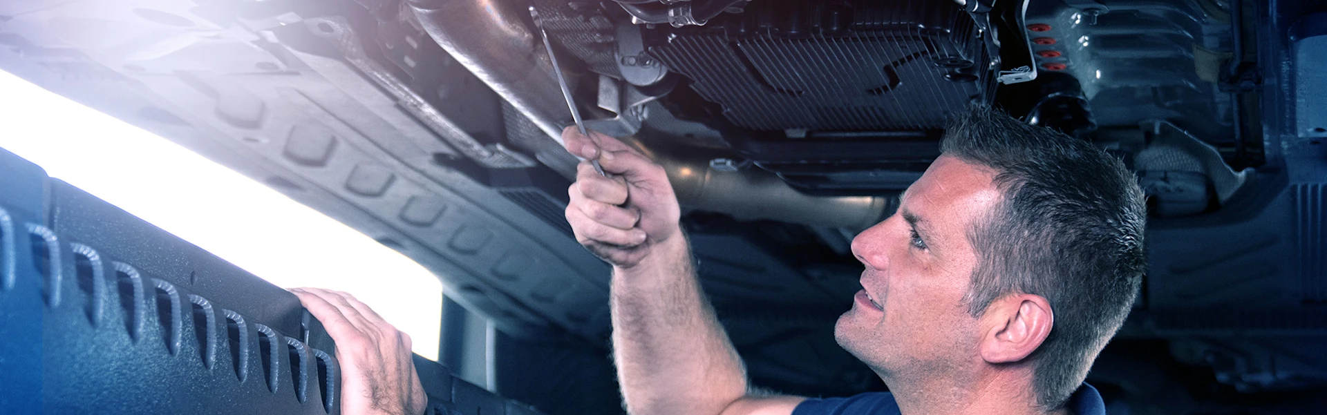 A mechanic stands under a car and tightens screws.