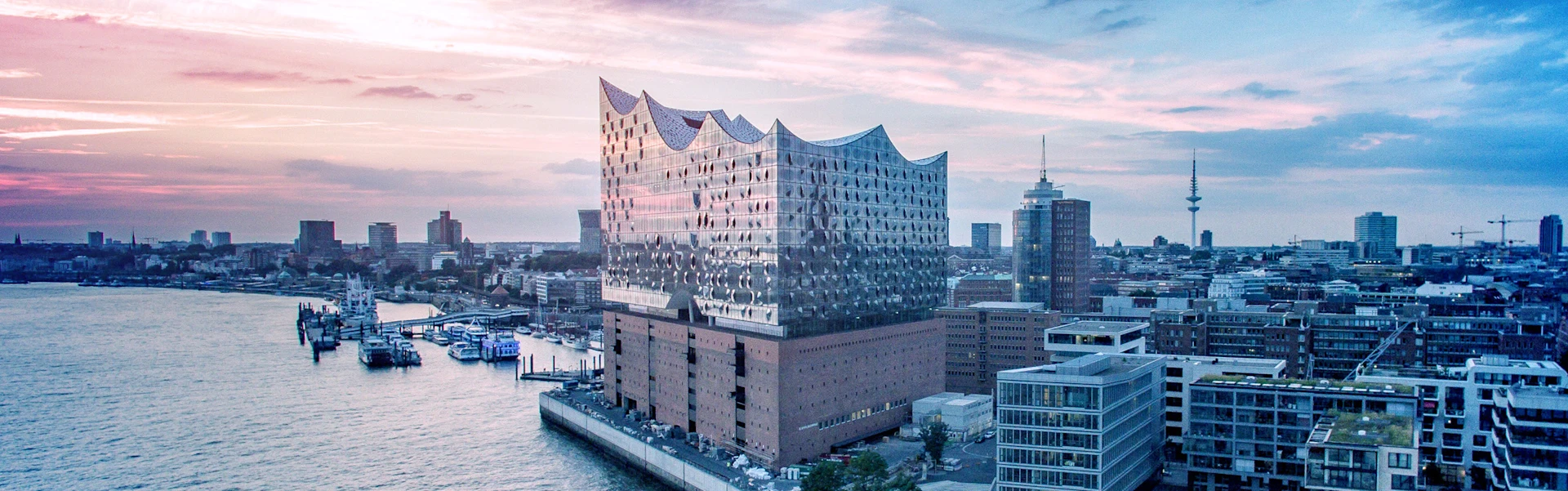 Photo of the Elbphilharmonie concert hall with the port of Hamburg in the background.