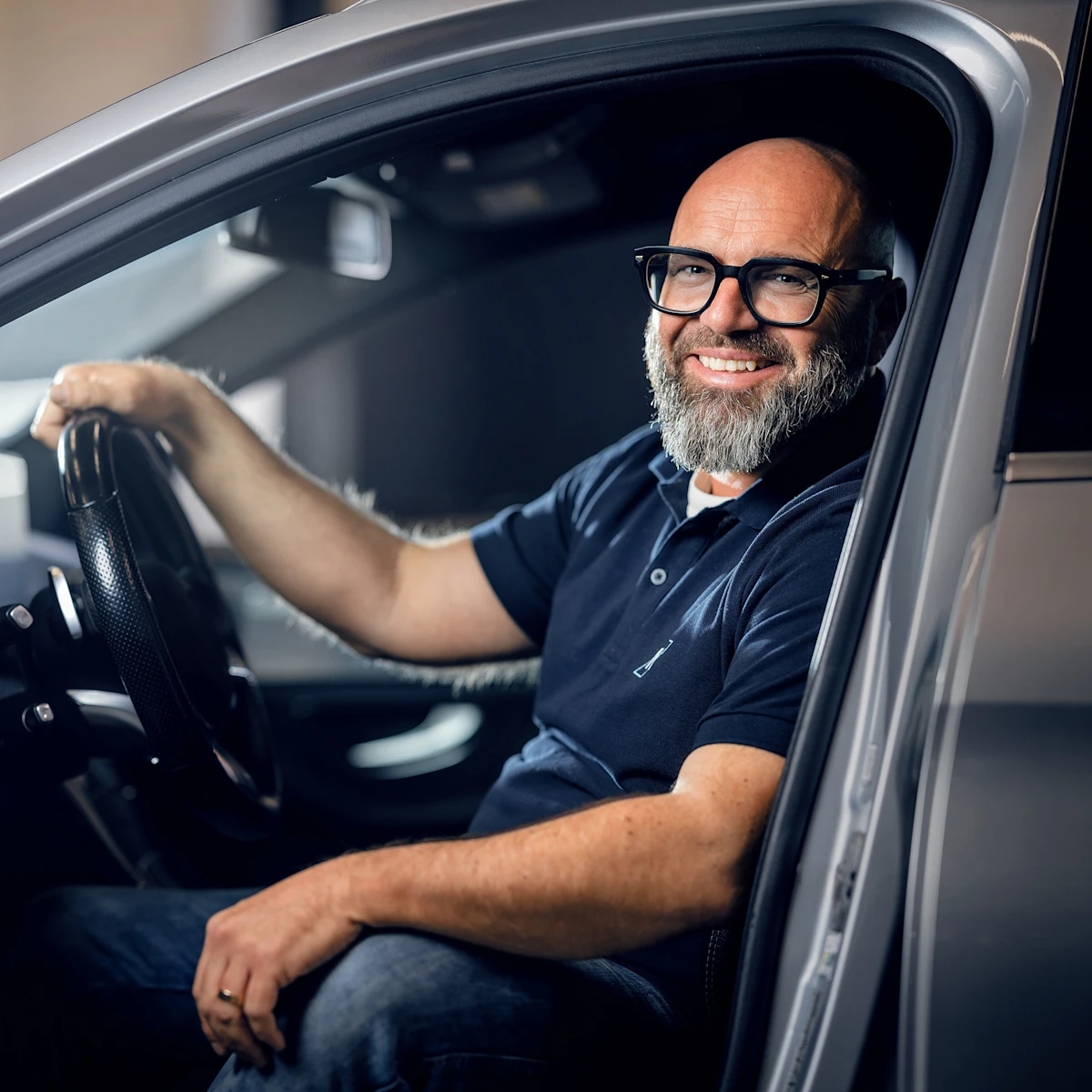 Der bekannte deutsche Mechaniker Andreas Raulfs, ist in einer Werkstatt, sitzt in einem Fahrzeug und lächelt in die Kamera.