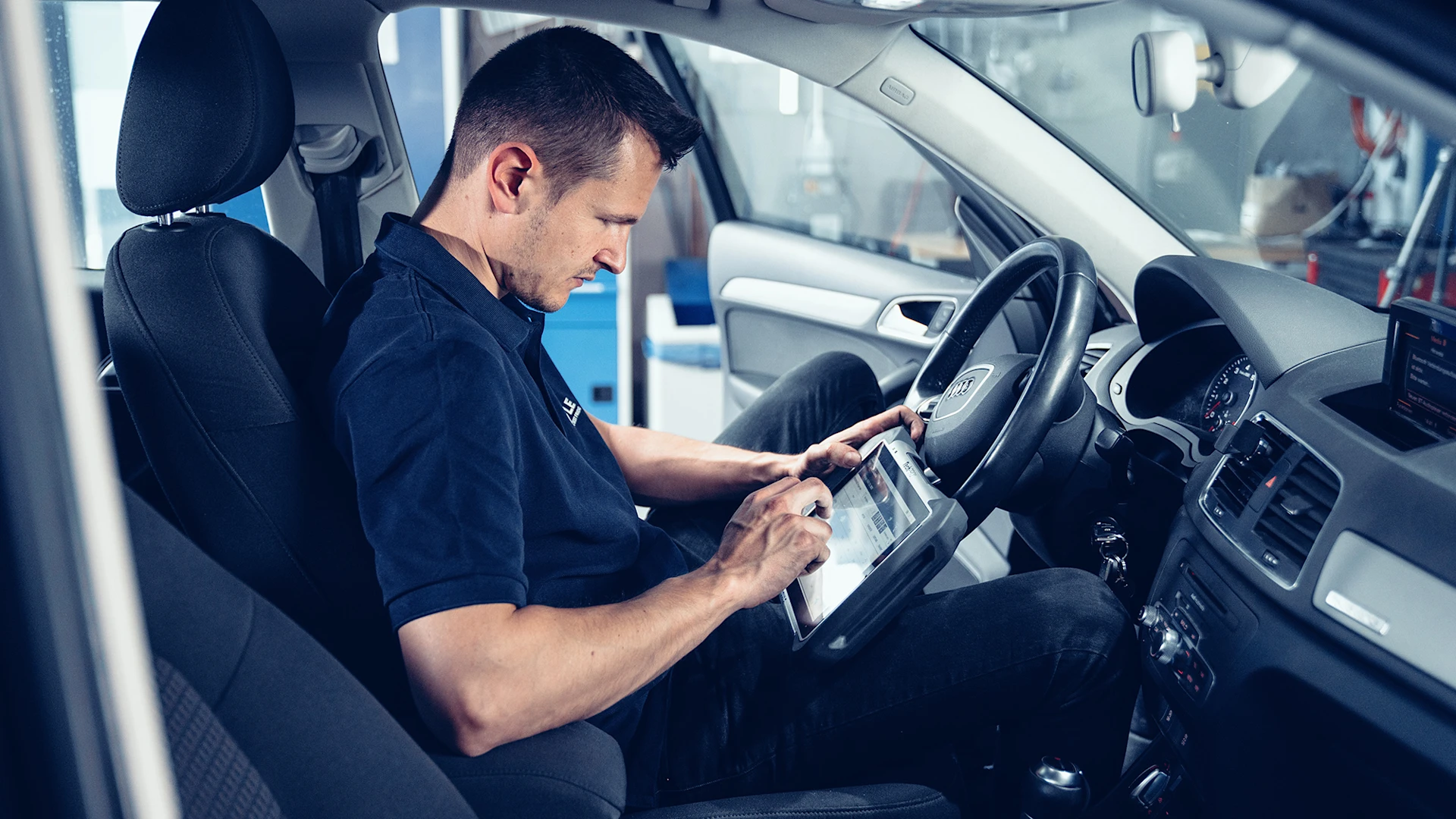 Person sitzt im Auto in einer Werkstatt und überprüft Daten am Tablet.