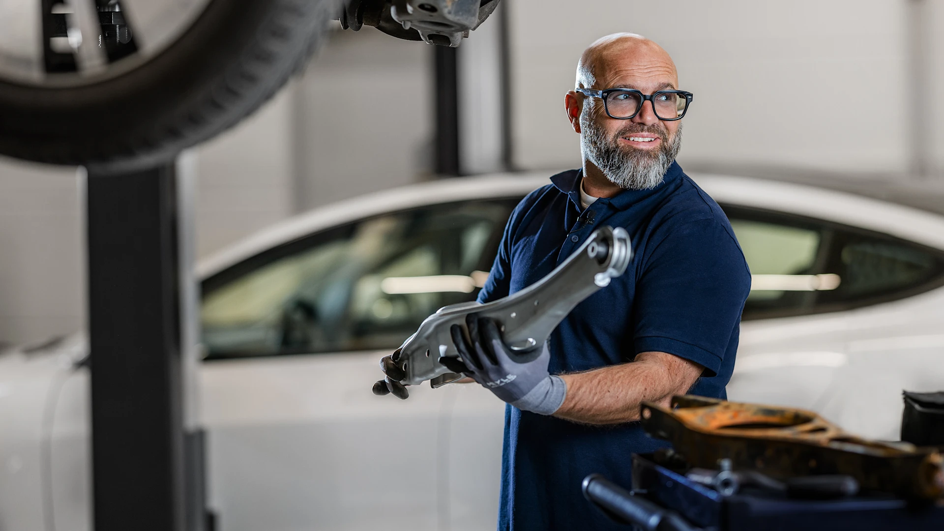 Der bekannte deutsche Mechaniker Andreas Raulfs, ist in einer Werkstatt an einer Hebebühne und hält ein Lenkungsteil.