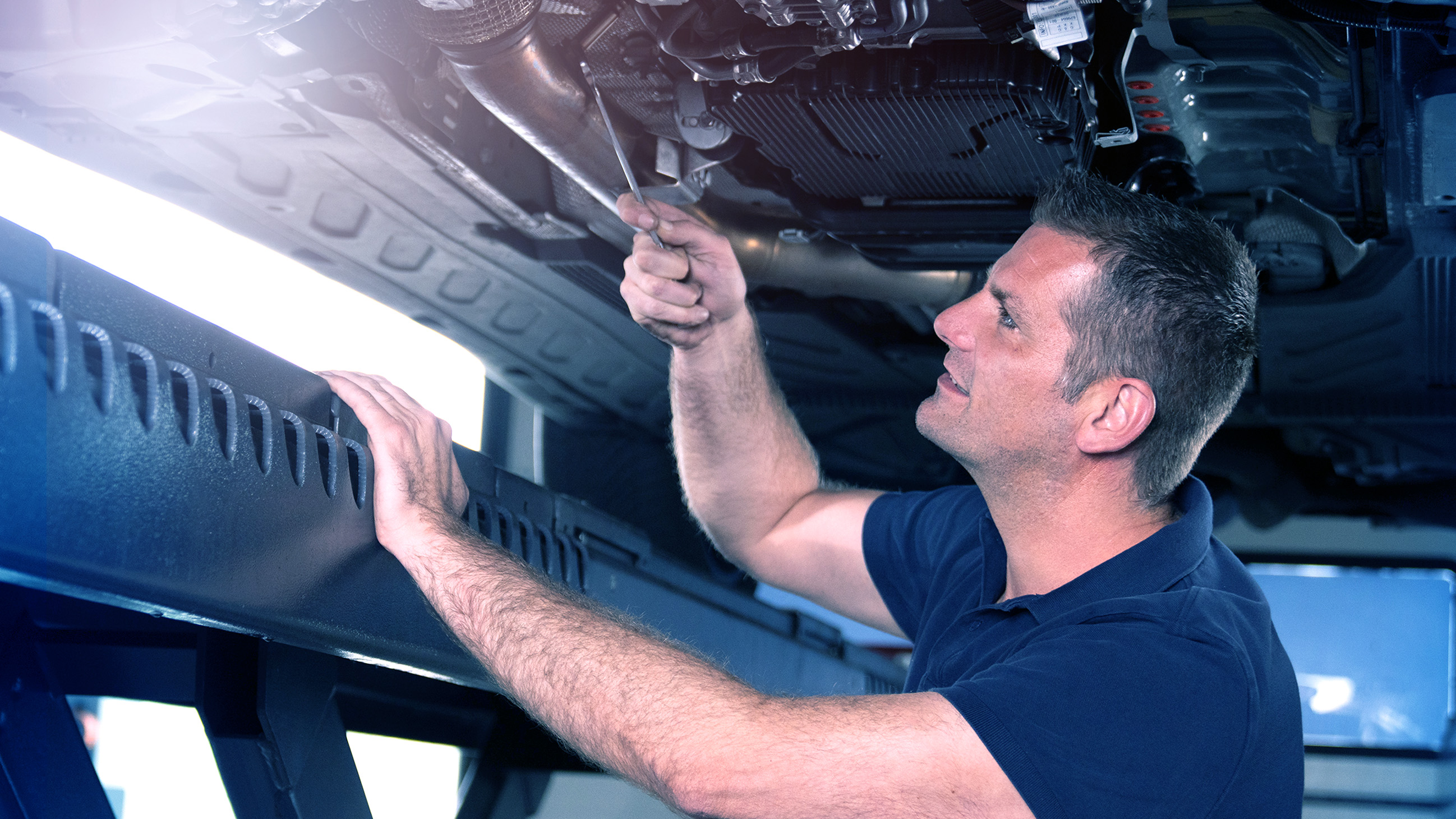 A mechanic stands under a car and tightens screws.