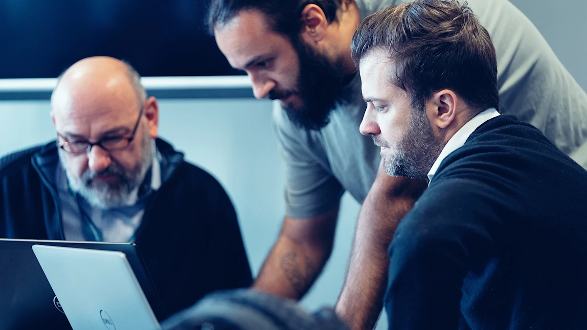 Three people look at laptops together and define technical specifications, requirements and improvements.