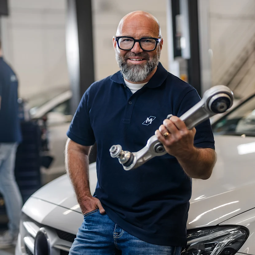 The well-known German mechanic Andreas Raulfs is standing in front of a car, holding a MEYLE HD handlebar and smiling into the camera.