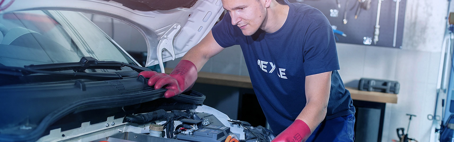 Person wearing protective gloves bends over open electric motor compartment.