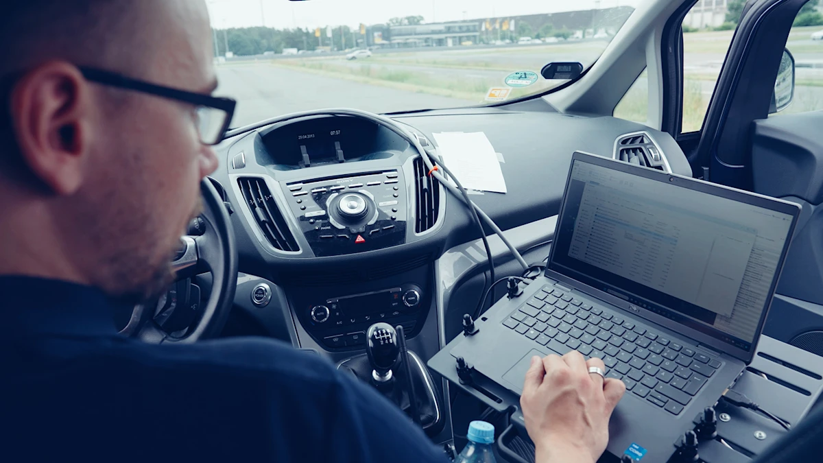 Person sits in the car and looks at a laptop connected to the car.