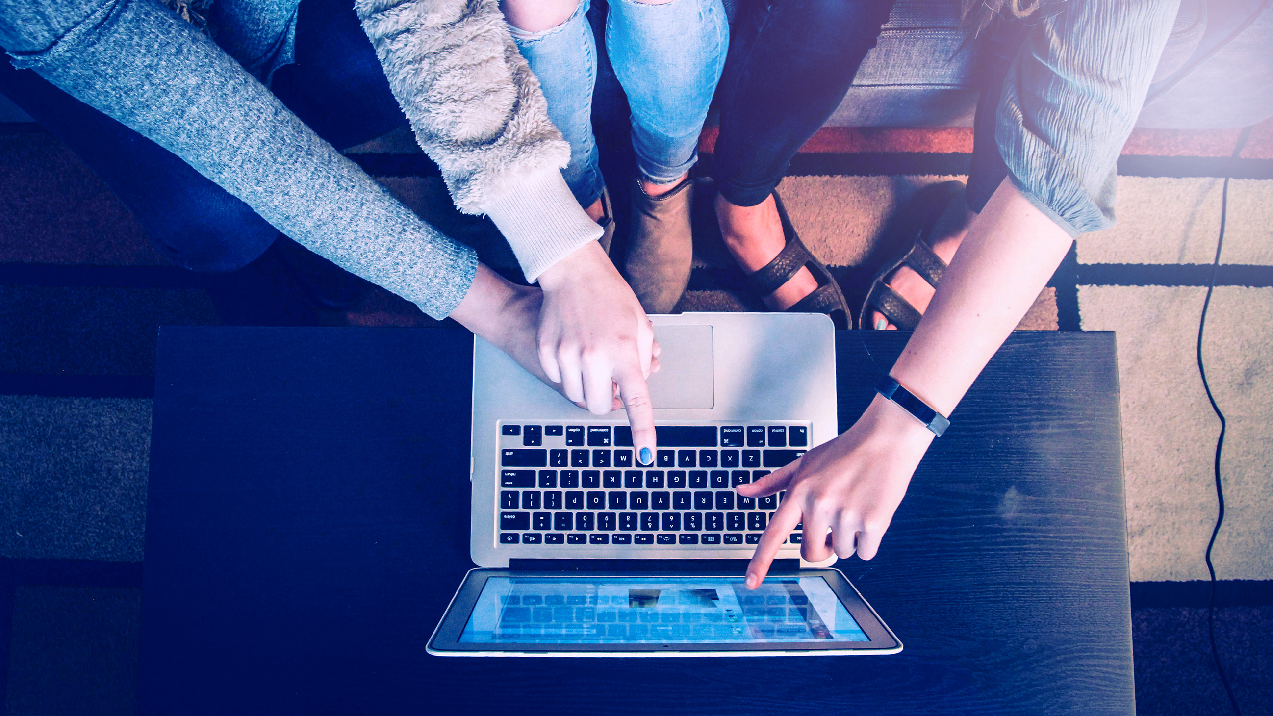 Keyboard of a laptop from above with fingers pointing at the screen. 
