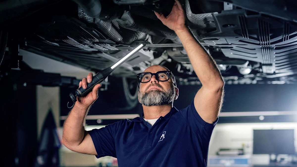 Andreas Raulf steht mit einer Werstattlampe unter einem Auto.