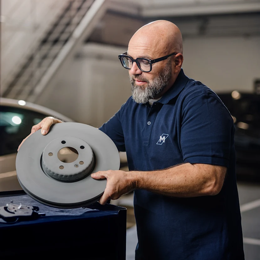 The well-known German mechanic Andreas Raulfs is standing in front of a car holding a MEYLE PD brake disk.