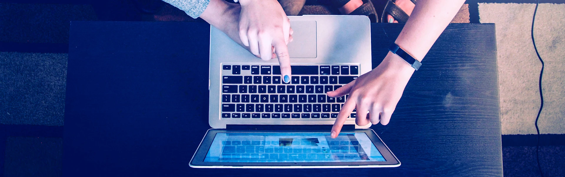 Keyboard of a laptop from above with fingers pointing at the screen.