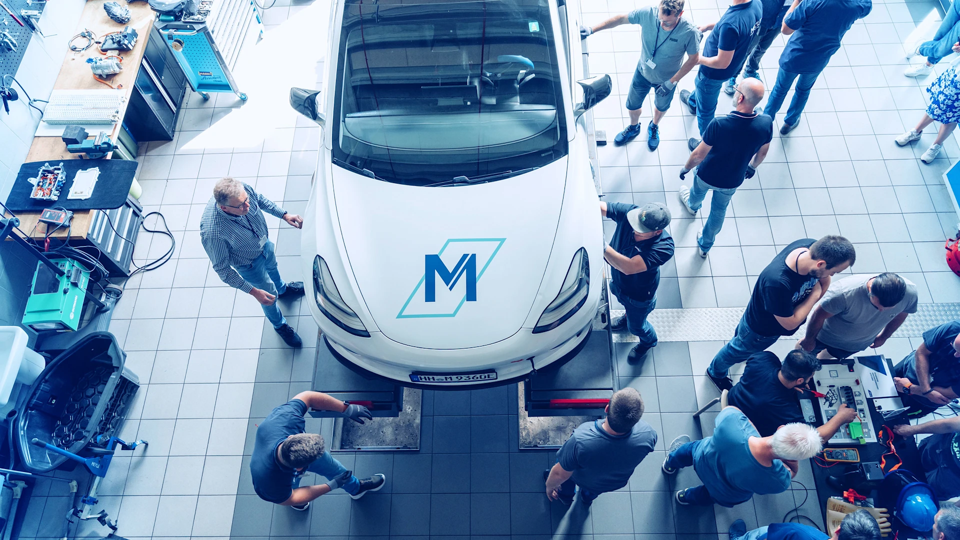 Top view of an electric vehicle in a workshop surrounded by technicians performing high-voltage diagnostics and battery assessment.