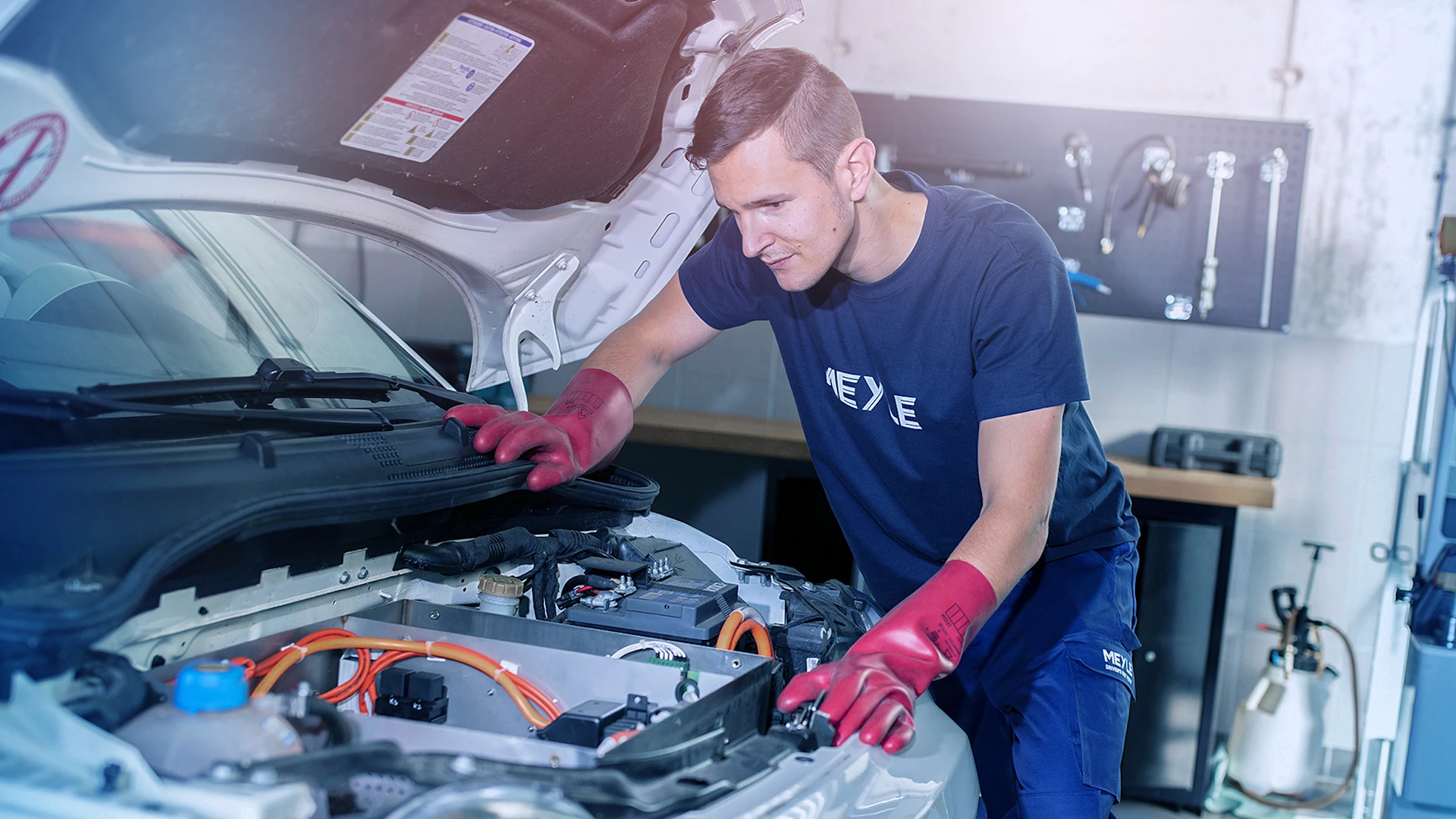 Person wearing protective gloves bends over open electric motor compartment.