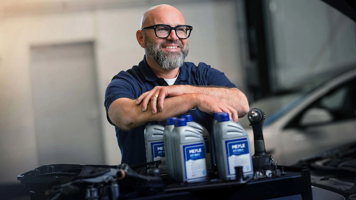 Andreas Raulf leans on MEYLE oil bottles in a workshop.