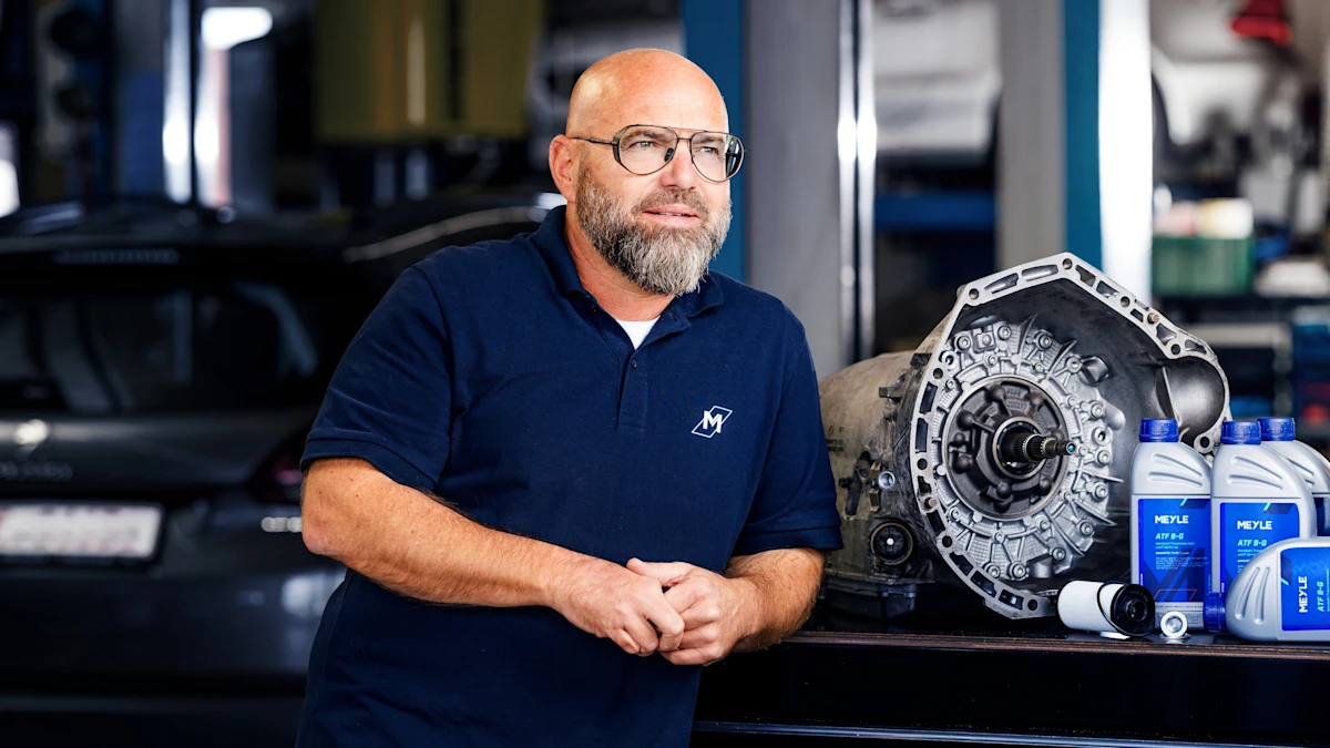 Andreas Raulf leans on MEYLE oil bottles in a workshop.