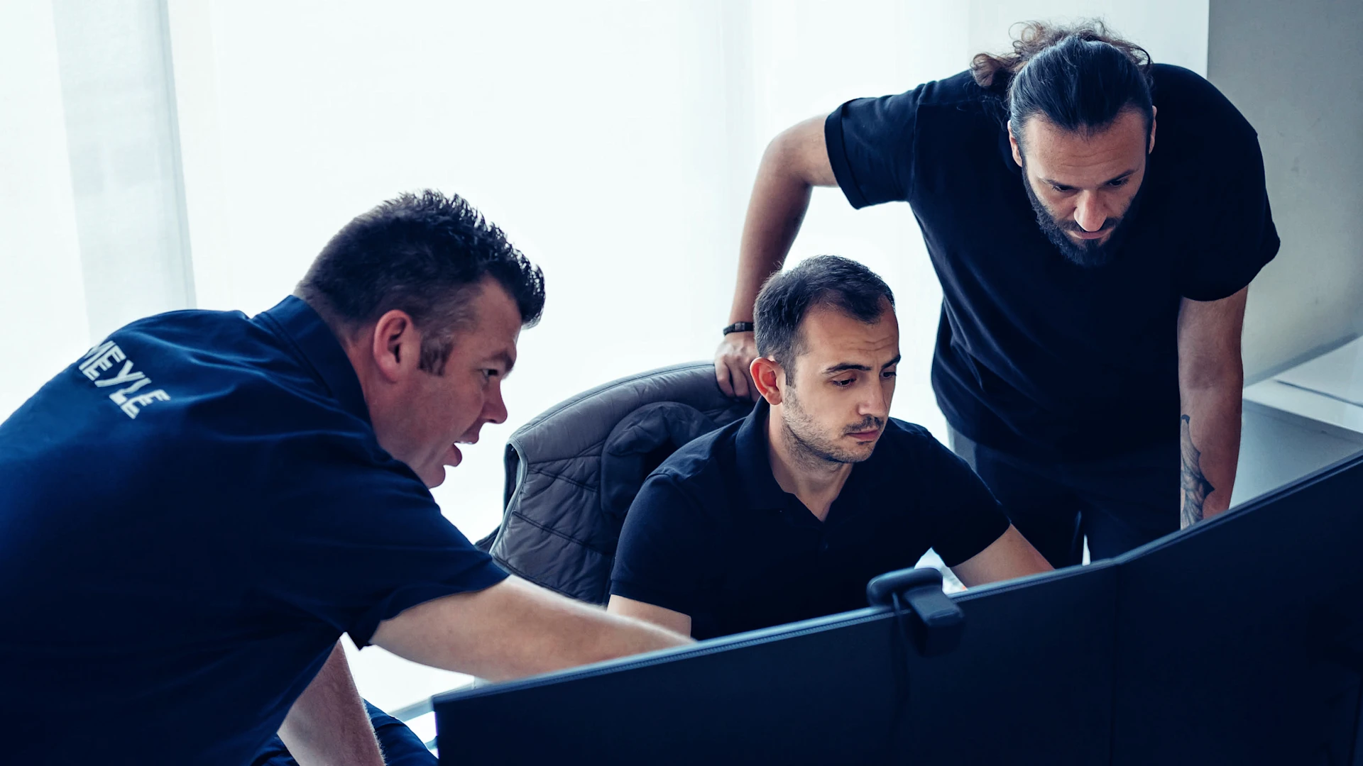 Three MEYLE colleagues work together in front of a screen, one person shows the others something.