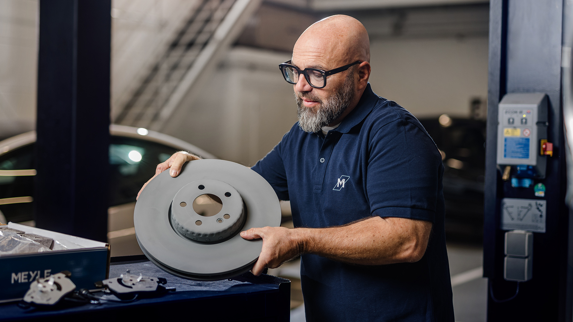 The well-known German mechanic Andreas Raulfs is standing in front of a car holding a MEYLE PD brake disk.