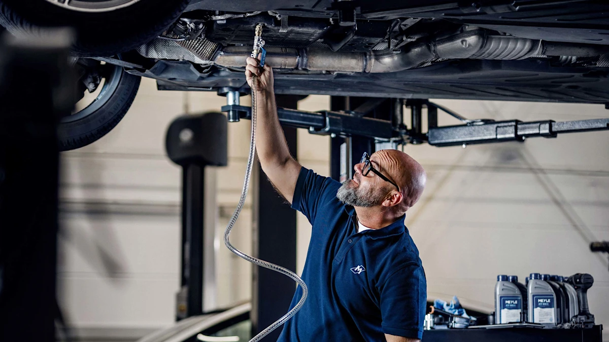 Andreas Raulf stands under a car and holds the MEYLE filling device.